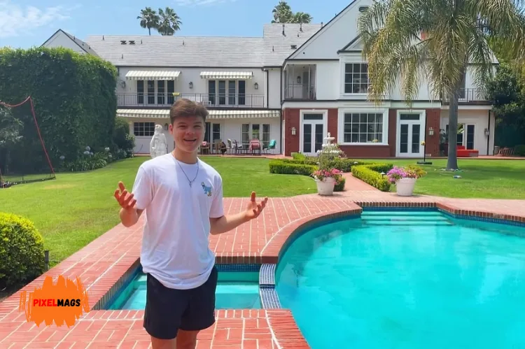 Jack Doherty stands smiling with his arms open near a bright blue swimming pool.
