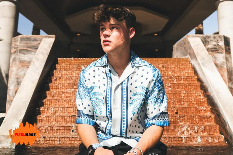Jack Doherty with tousled brown hair sits in front of a cascading brick water fountain.