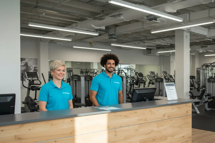 Modern, well-lit gym with welcoming staff at the front desk.