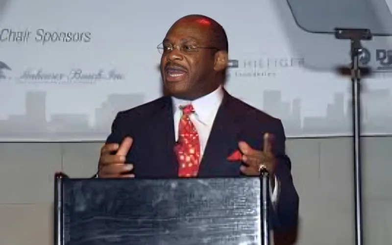 willie gary in a suit and red tie speaking at a podium during a formal event.