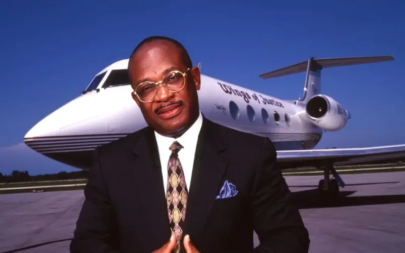 Willie E. Gary in suit standing before private jet on runway.
