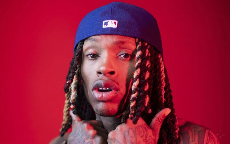 Rapper King Von looking forward while wearing a blue baseball cap against a vibrant red background.