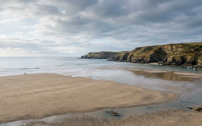 Wide sandy beach at low tide near Padstow, calm sea, dramatic coastal scenery, peaceful atmosphere.